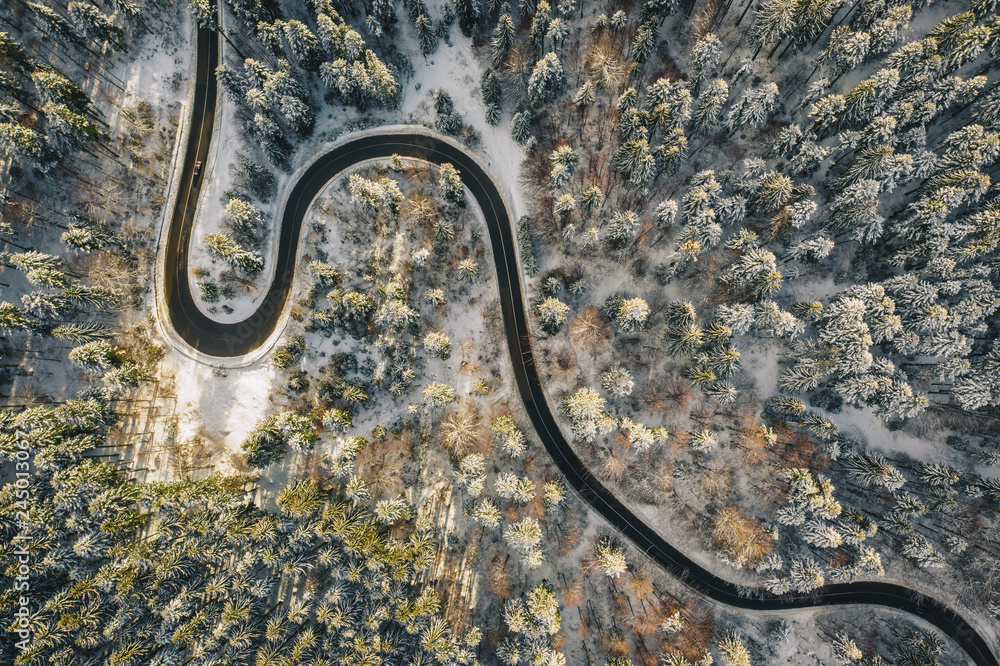 Drone aerial view of a winding road in the middle of the forest with snow on trees