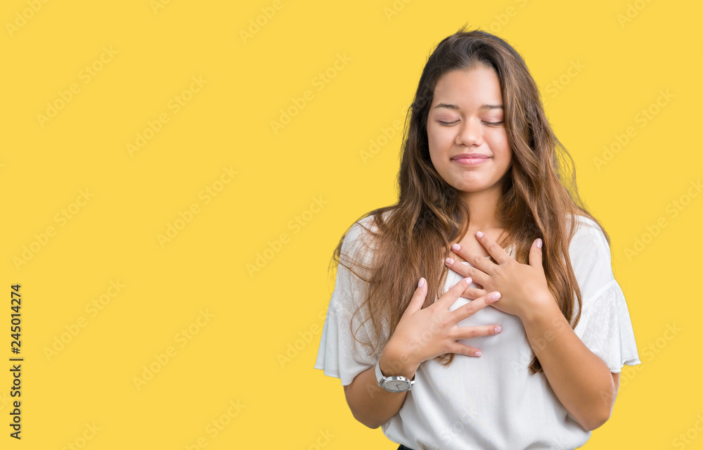 Young beautiful brunette business woman over isolated background smiling with hands on chest with closed eyes and grateful gesture on face. Health concept. Young beautiful brunette business woman over isolated background smiling with hands on chest with closed eyes and grateful gesture on face. Health concept.