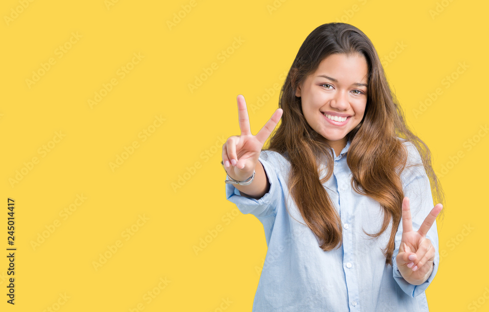 Young beautiful brunette business woman over isolated background smiling looking to the camera showing fingers doing victory sign. Number two. Young beautiful brunette business woman over isolated background smiling looking to the camera showing fingers doing victory sign. Number two.
