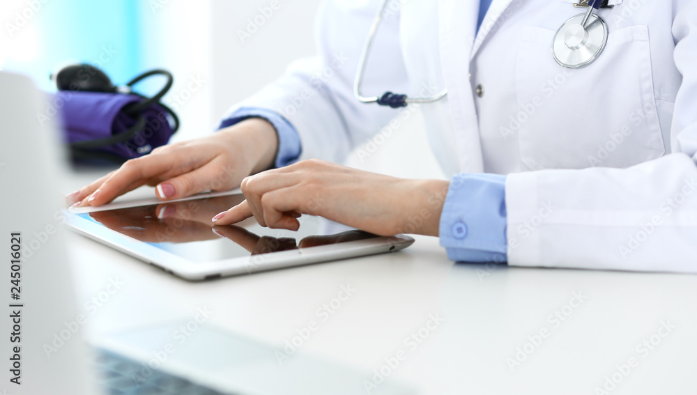 Woman doctor using tablet computer while sitting in hospital office closeup. Healthcare, insurance and medicine concept Woman doctor using tablet computer while sitting in hospital office closeup. Healthcare, insurance and medicine concept