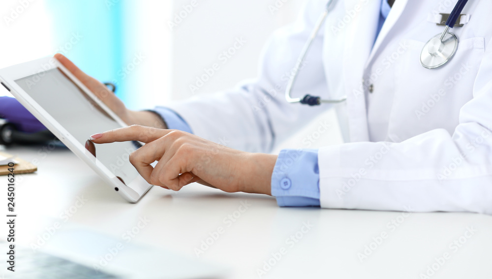 Woman doctor using tablet computer while sitting in hospital office closeup. Healthcare, insurance and medicine concept Woman doctor using tablet computer while sitting in hospital office closeup. Healthcare, insurance and medicine concept