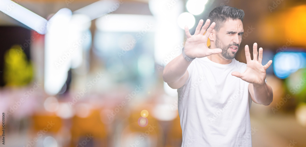 Young man wearing casual white t-shirt over isolated background afraid and terrified with fear expression stop gesture with hands, shouting in shock. Panic concept. Young man wearing casual white t-shirt over isolated background afraid and terrified with fear expression stop gesture with hands, shouting in shock. Panic concept.