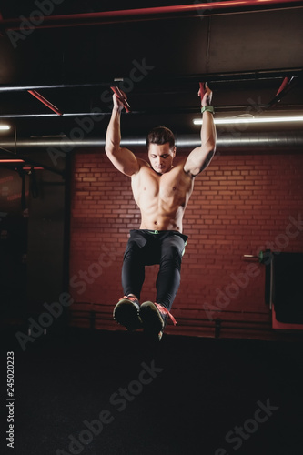 Athletic man turbo sit-ups pull on horizontal bar. Naked in black pants.