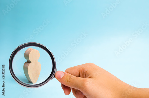 Magnifying glass is looking at the Wooden figurine of a man on a blue background. A lonely man, minimalism. Place for text. Slide for presentation.