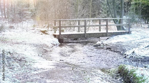 Im Winterwald fließt ein Fluß. Es ist die Glenne bei Rixen im Sauerland. Eine Holzbrücke überquert den Fluss. Sound. Die Naturlandschaft ist mit Schnee bedeckt. photo