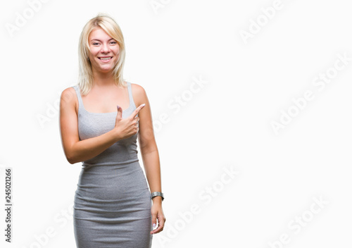 Young beautiful blonde woman over isolated background cheerful with a smile of face pointing with hand and finger up to the side with happy and natural expression on face looking at the camera. © Krakenimages.com