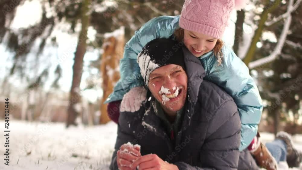 Girl plays snowballs with his father, they are lying in the snow and laughing merrily. Happy family holidays Girl plays snowballs with his father, they are lying in the snow and laughing merrily. Happy family holidays