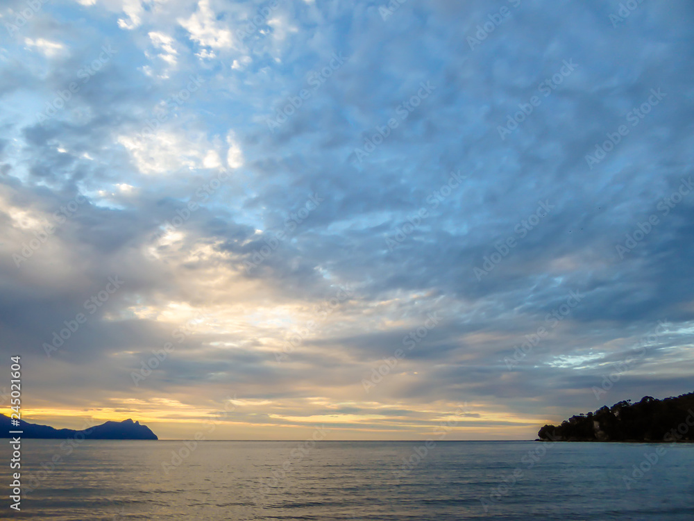Beautiful formation of clouds over the sea in Bako National Park, Borneo, Malaysia during the sunset. Blue and yellow sky. Two islands visible on both sides of the picture. Overcast. 