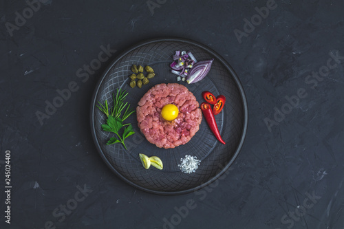 Steak tartare with yolk and ingredients on black ceramic plate
