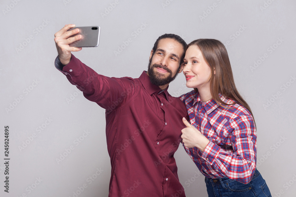 Φωτογραφία Portrait of happy satisfied couple standing, looking and smiling at camera of mobile smart phone to make selfie or video call with thumbs up