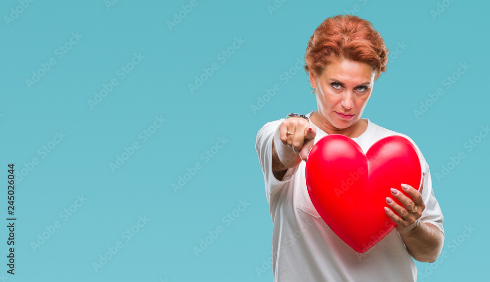 Senior caucasian woman holding red heart in love over isolated background pointing with finger to the camera and to you, hand sign, positive and confident gesture from the front Senior caucasian woman holding red heart in love over isolated background pointing with finger to the camera and to you, hand sign, positive and confident gesture from the front