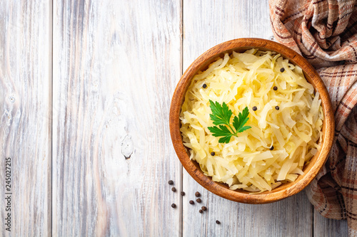 Homemade sauerkraut with black pepper and parsley in wooden bowl on rustic background. Top view. Copy space.