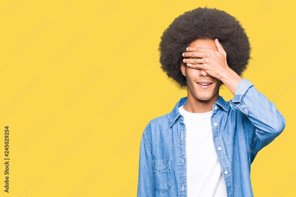 Young african american man with afro hair smiling and laughing with hand on face covering eyes for surprise. Blind concept. Young african american man with afro hair smiling and laughing with hand on face covering eyes for surprise. Blind concept.
