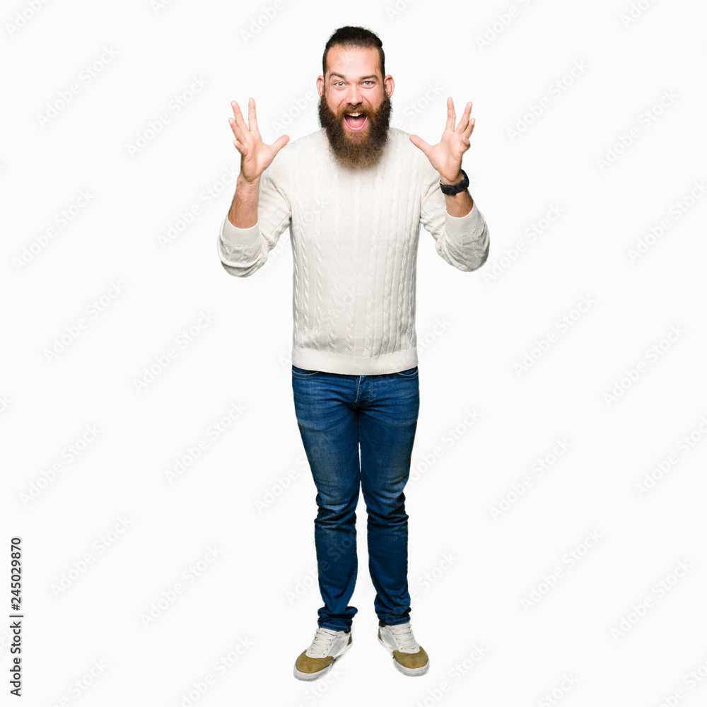 Young hipster man wearing winter sweater celebrating crazy and amazed for success with arms raised and open eyes screaming excited. Winner concept Young hipster man wearing winter sweater celebrating crazy and amazed for success with arms raised and open eyes screaming excited. Winner concept
