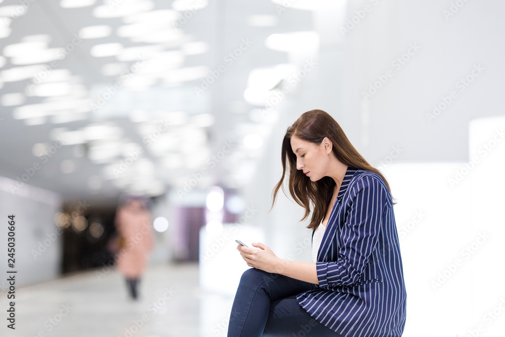 Girl in suit surfs the Internet in the phone sitting on a bench in the metro at the station of underground transport