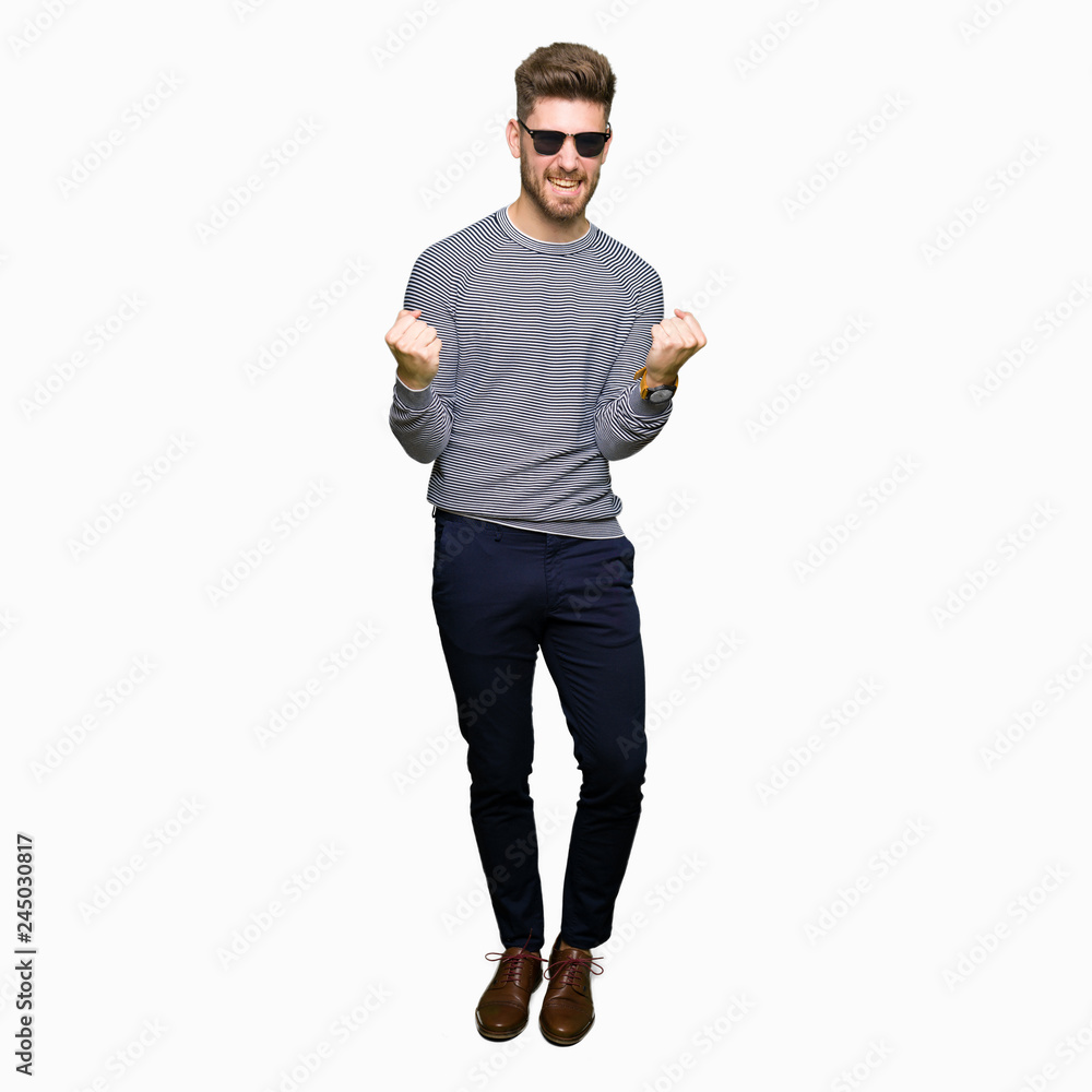 Young handsome man wearing sunglasses very happy and excited doing winner gesture with arms raised, smiling and screaming for success. Celebration concept. Young handsome man wearing sunglasses very happy and excited doing winner gesture with arms raised, smiling and screaming for success. Celebration concept.