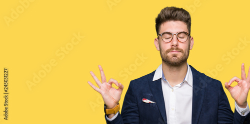 Young handsome business man wearing glasses relax and smiling with eyes closed doing meditation gesture with fingers. Yoga concept.