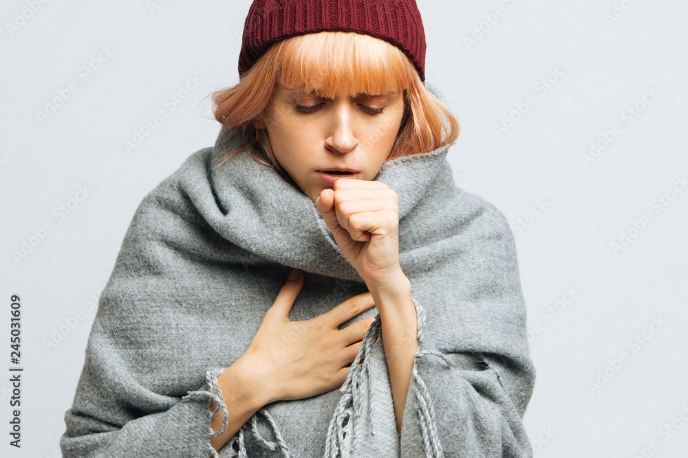 Cute sick young teen woman in red hat, wrapped in warm scarf coughing