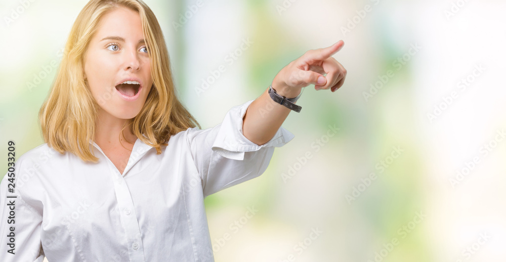 Beautiful young business woman over isolated background Pointing with finger surprised ahead, open mouth amazed expression, something in front