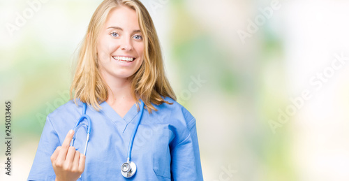 Beautiful young doctor woman wearing medical uniform over isolated background Beckoning come here gesture with hand inviting happy and smiling