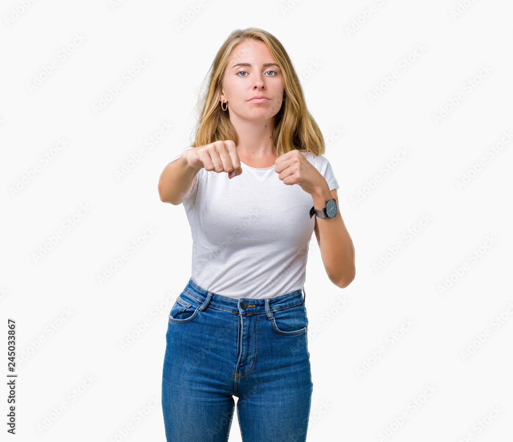 Beautiful young woman wearing casual white t-shirt over isolated background Punching fist to fight, aggressive and angry attack, threat and violence Beautiful young woman wearing casual white t-shirt over isolated background Punching fist to fight, aggressive and angry attack, threat and violence