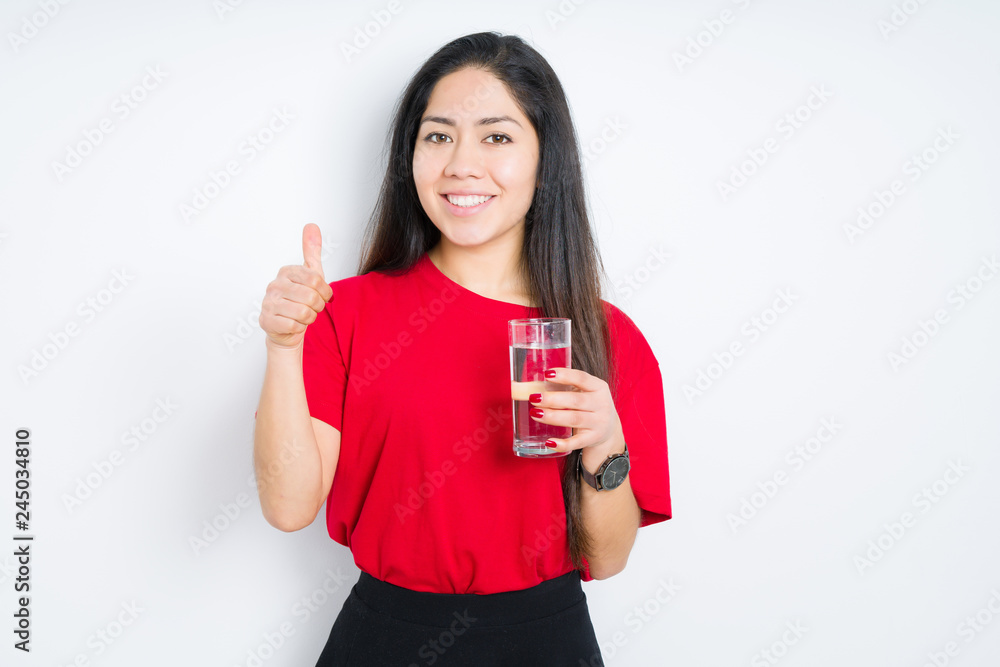 Young brunette woman drinking a glass of water over isolated background happy with big smile doing ok sign, thumb up with fingers, excellent sign Young brunette woman drinking a glass of water over isolated background happy with big smile doing ok sign, thumb up with fingers, excellent sign