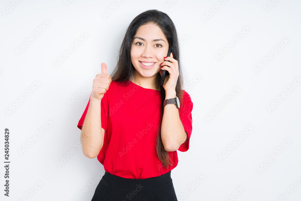 Young brunette woman talking on smartphone over isolated background happy with big smile doing ok sign, thumb up with fingers, excellent sign Young brunette woman talking on smartphone over isolated background happy with big smile doing ok sign, thumb up with fingers, excellent sign