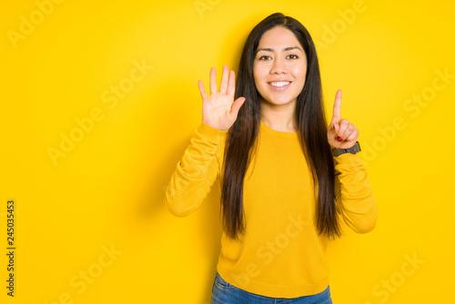 Beautiful brunette woman over yellow isolated background showing and pointing up with fingers number six while smiling confident and happy.