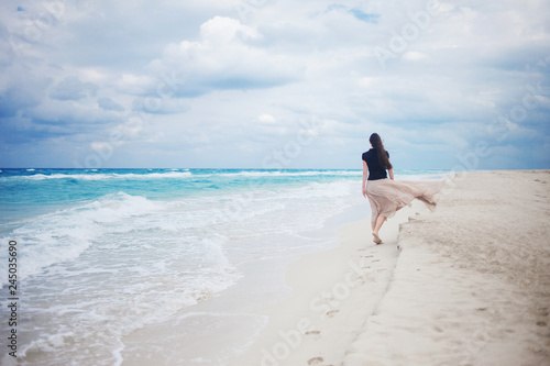 Back view of young woman in a long skirt walking on the ocean. 