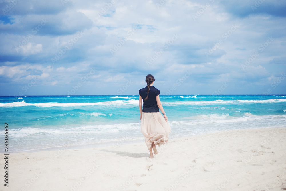 Back view of young woman in a long skirt walking on the ocean. 