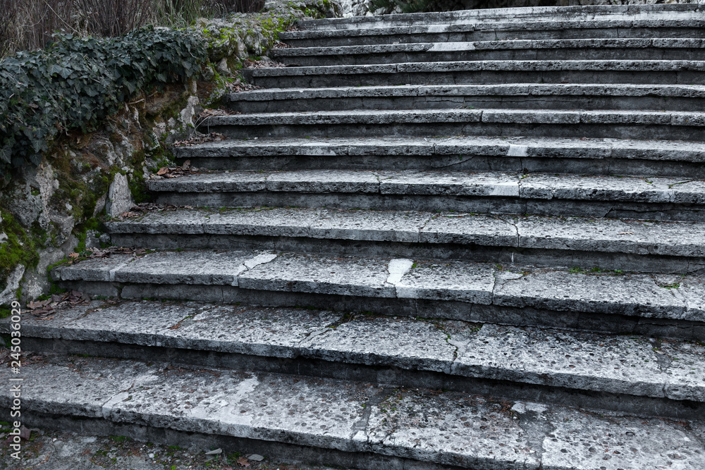An old open outer stone staircase. Stone, cement steps of the old staircase with traces of weathering and destruction. An ancient stone staircase, ancient broken worn steps. Selective focus An old open outer stone staircase. Stone, cement steps of the old staircase with traces of weathering and destruction. An ancient stone staircase, ancient broken worn steps. Selective focus