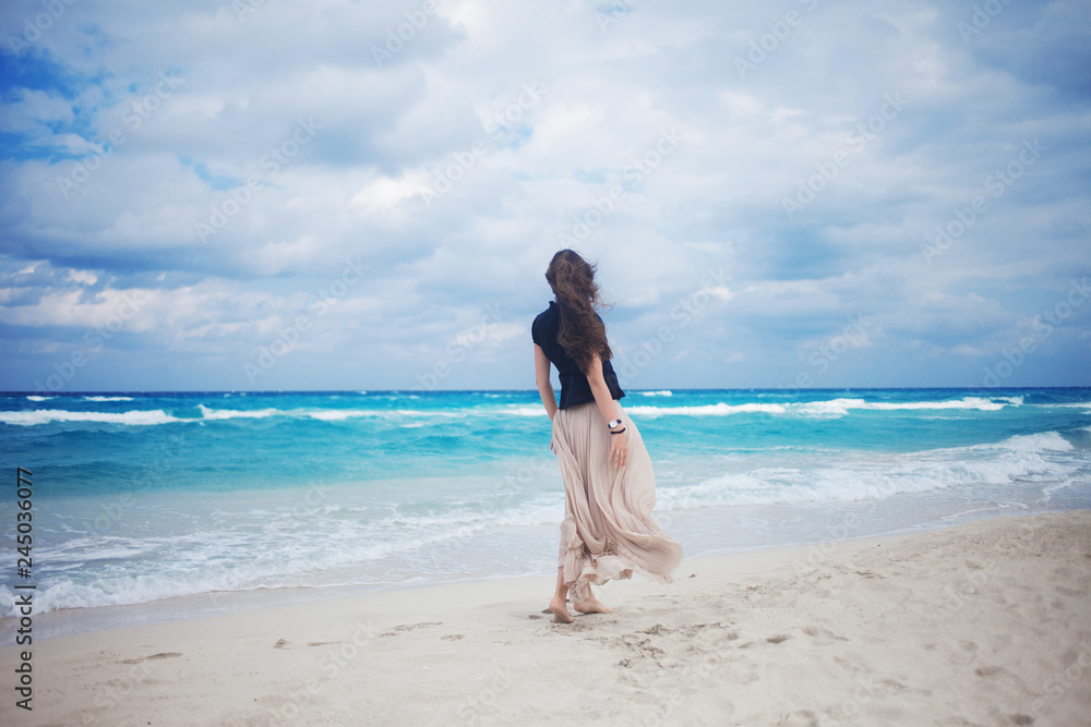 Back view of young woman in a long skirt walking on the ocean. 