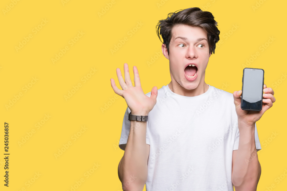 Young man showing smartphone screen over isolated background very happy and excited, winner expression celebrating victory screaming with big smile and raised hands Young man showing smartphone screen over isolated background very happy and excited, winner expression celebrating victory screaming with big smile and raised hands