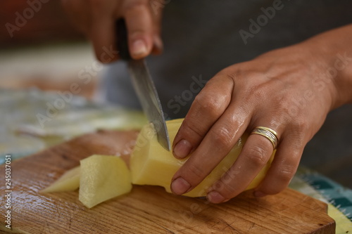 Woman's hand with a knife cutting slicing potatoes on wooden board in kitchen.