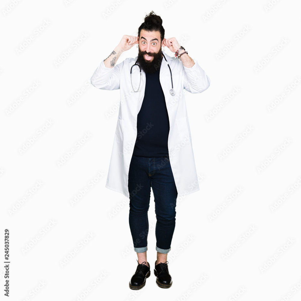 Doctor with long hair wearing medical coat and stethoscope Smiling pulling ears with fingers, funny gesture. Audition problem Doctor with long hair wearing medical coat and stethoscope Smiling pulling ears with fingers, funny gesture. Audition problem