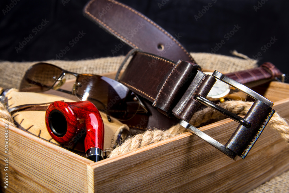 Men's accessories with brown leather belt, sunglasses, watch, smoking pipe  and bottle with perfume on rustic background. Stock Photo