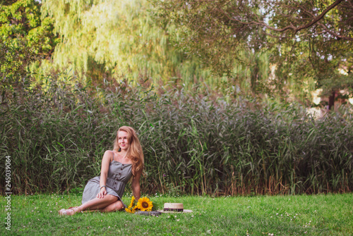 Beautiful woman with long blond hair walking in the park with sunflowers bouquet, green grass, summertime © milenie