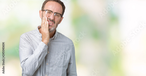 Handsome middle age elegant senior man wearing glasses over isolated background touching mouth with hand with painful expression because of toothache or dental illness on teeth. Dentist concept. © Krakenimages.com