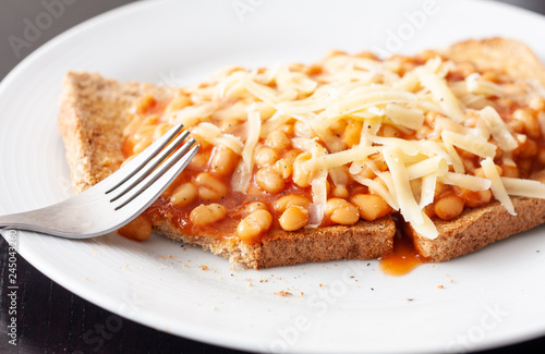 Partially eaten meal of baked beans on toast topped with grated cheese