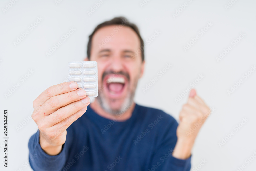 Senior man holding pharmaceutical pills over isolated background screaming proud and celebrating victory and success very excited, cheering emotion Senior man holding pharmaceutical pills over isolated background screaming proud and celebrating victory and success very excited, cheering emotion