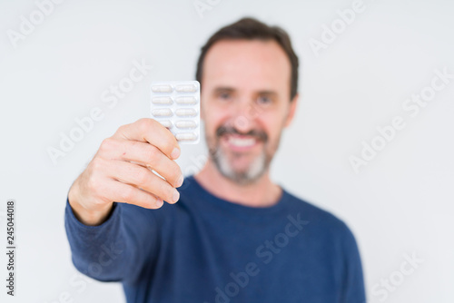 Senior man holding pharmaceutical pills over isolated background with a happy face standing and smiling with a confident smile showing teeth