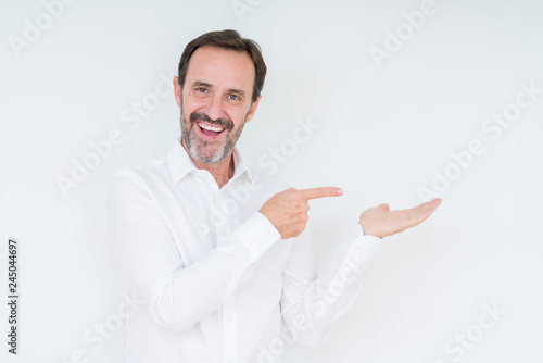 Elegant senior man over isolated background amazed and smiling to the camera while presenting with hand and pointing with finger.