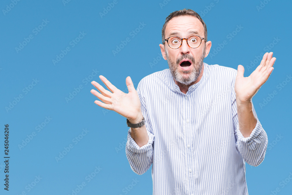 Fototapeta premium Middle age hoary senior man wearing glasses over isolated background clueless and confused expression with arms and hands raised. Doubt concept.