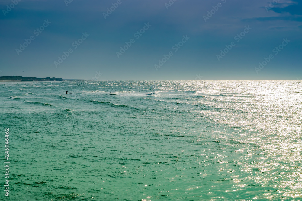 Obraz premium View of the beautiful scenic sea, reflecting sun, dark storm clouds and two people swimming in the distance on a paddle board.North sea in France.