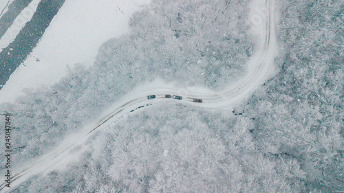 Top view of cars riding on the curve snowy countryroad through the beautiful snow covered forest. Scenic landscpes. Drone shot