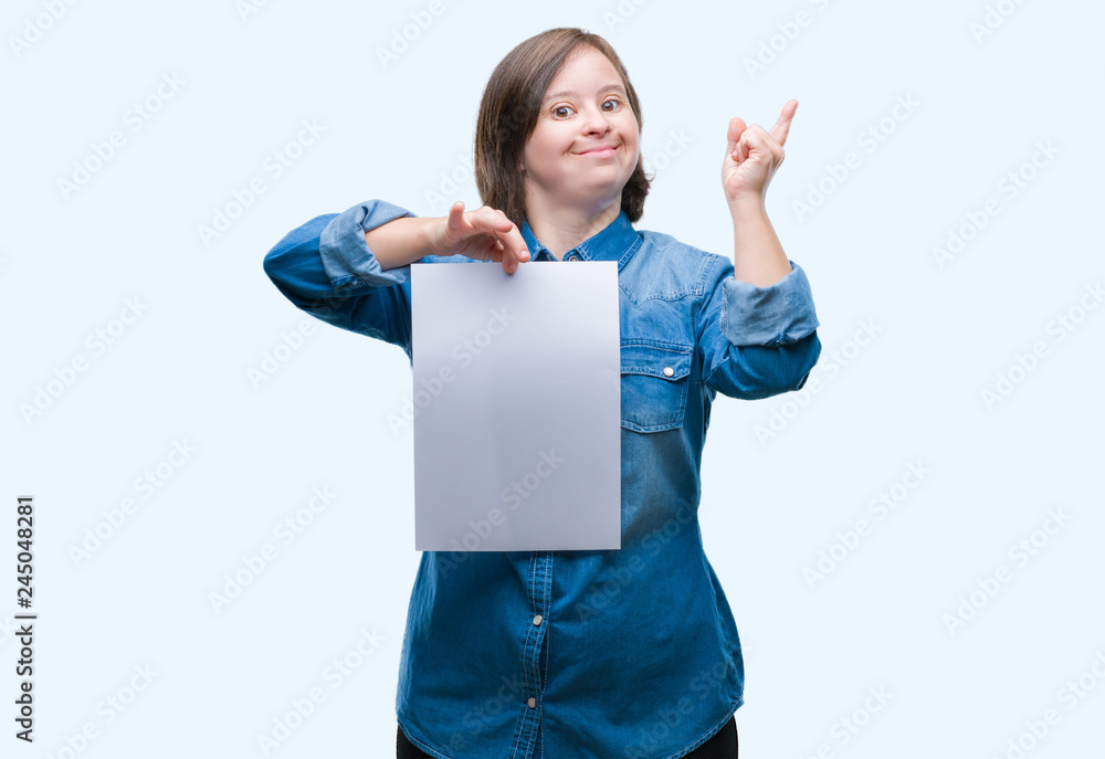 Young adult woman with down syndrome holding blank paper sheet over isolated background very happy pointing with hand and finger to the side Young adult woman with down syndrome holding blank paper sheet over isolated background very happy pointing with hand and finger to the side