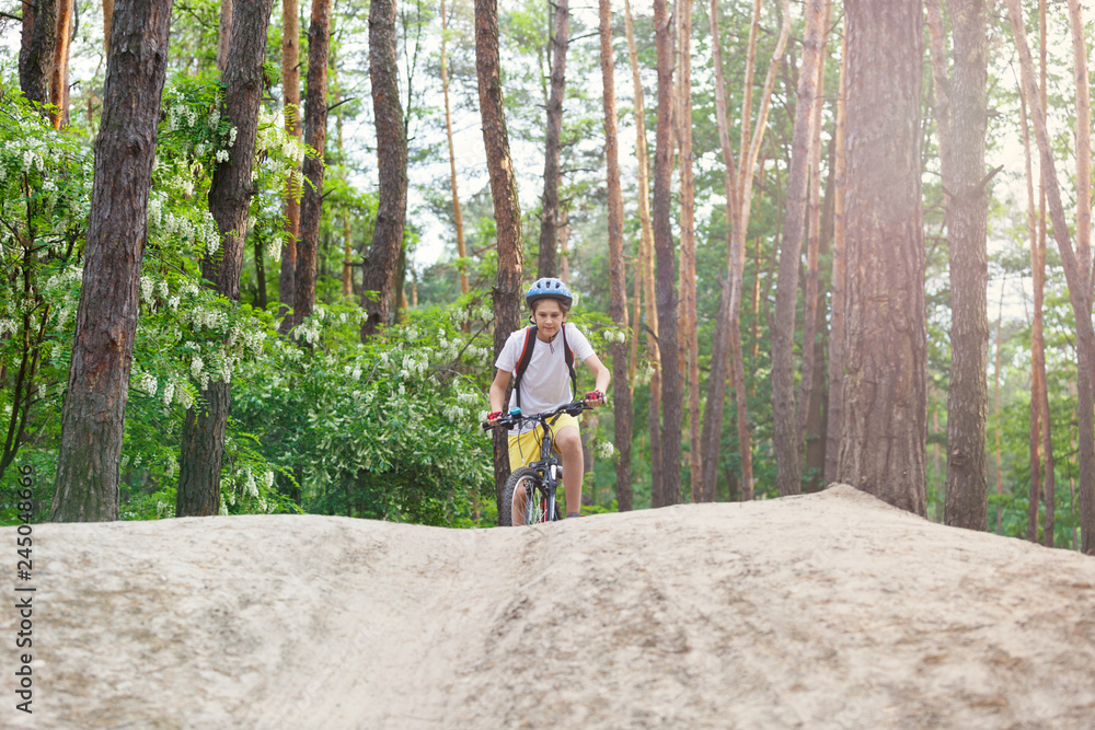 Obraz premium Child teenager on a bicycle ride in the forest at spring or summer. Boy cycling outdoors in helmet