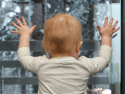 a little boy stands and looks out the window at the winter landscape. view from the back of a small child.