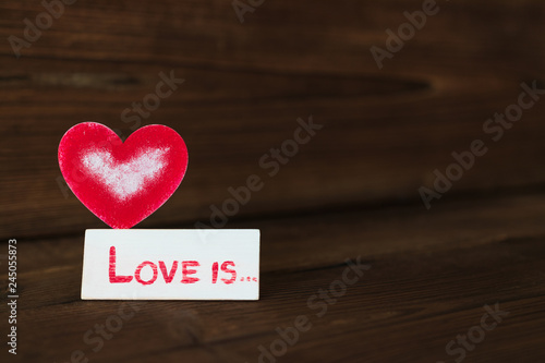 red heart on wooden background. Valentine's Day. celebration. the inscription on the plate "love is ..."