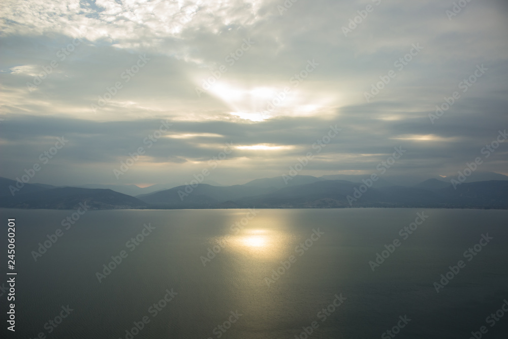 gray rainy and cloudy weather background landscape of morning sun rise time above lake calm water surface with mountain horizon silhouettes gray rainy and cloudy weather background landscape of morning sun rise time above lake calm water surface with mountain horizon silhouettes